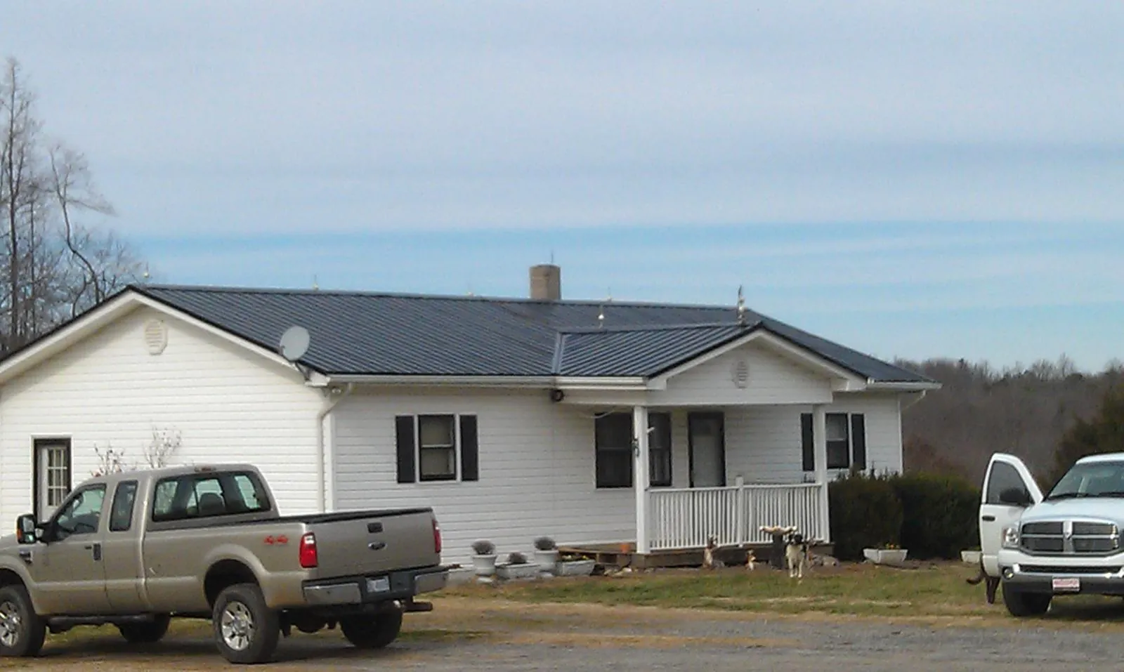 Finished dark metal roof on a white ranch home with work trucks parked in Cleveland